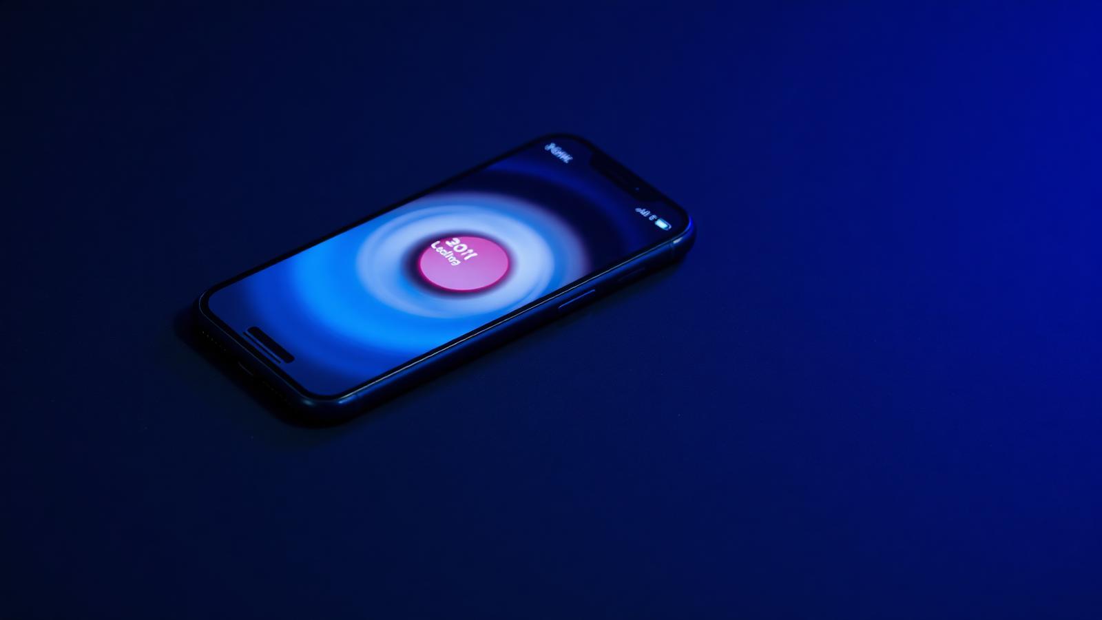 An iPhone glowing blue on a dark surface showing a loading animation
